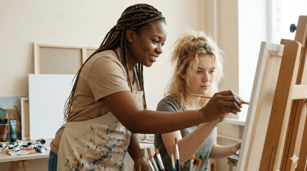 Two women painting together at an easel in an art studio
